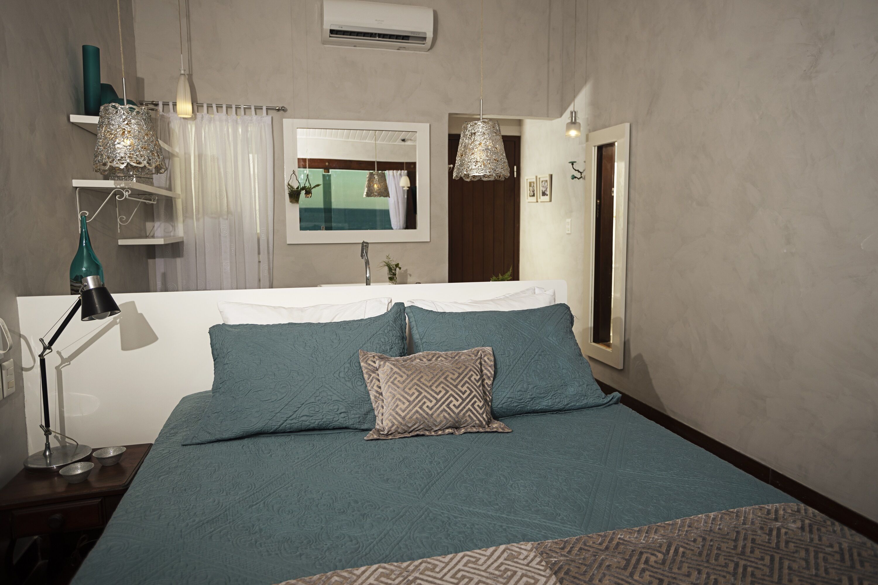 A bedroom with a bed, a bedside table with a lamp, a mirror, and a window with curtains.