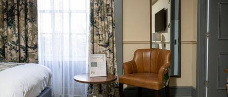 A hotel room with a bed, a chair, a small table, a mirror, and a door.