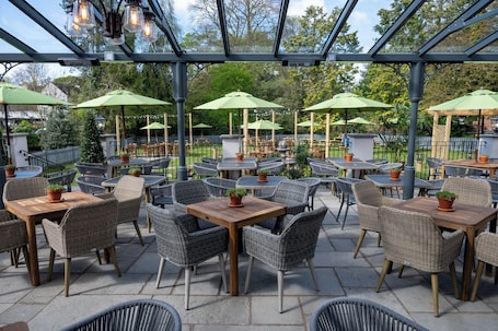 An outdoor patio area with wicker tables and chairs, green umbrellas, and potted plants.. Himley House Hotel by Chef and Brewer Collection