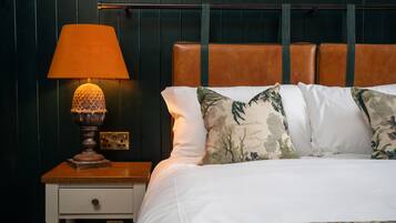 A neatly made bed with white linens and floral pillows, a wooden nightstand with a lamp, and a dark green wall with a wooden panel design.