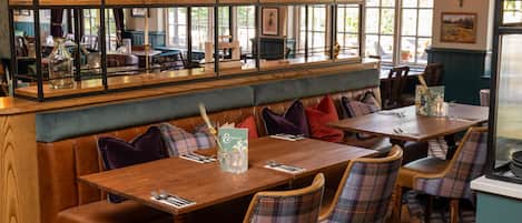 A restaurant with wooden tables, plaid chairs, and a bar area with shelves.