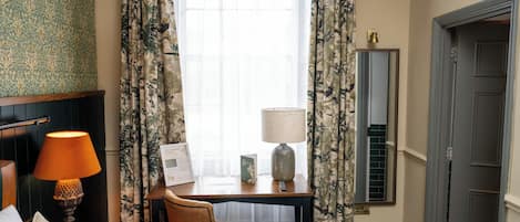 Habitación de hotel con cama, escritorio con lámpara, silla y ventana con cortinas.