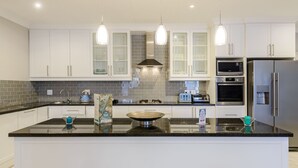 Uma cozinha moderna com armários brancos, bancada preta, eletrodomésticos de aço inoxidável e iluminação pendente.