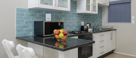 A modern kitchen with white cabinets, a microwave, a stove, and a bowl of fruit on the counter.