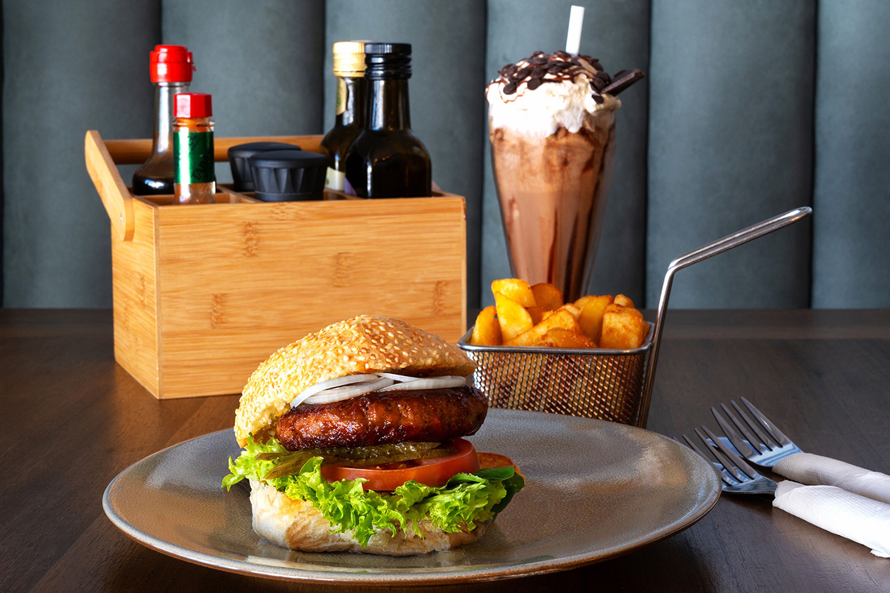 A plate with a burger and fries, a drink, and condiments in a wooden box.