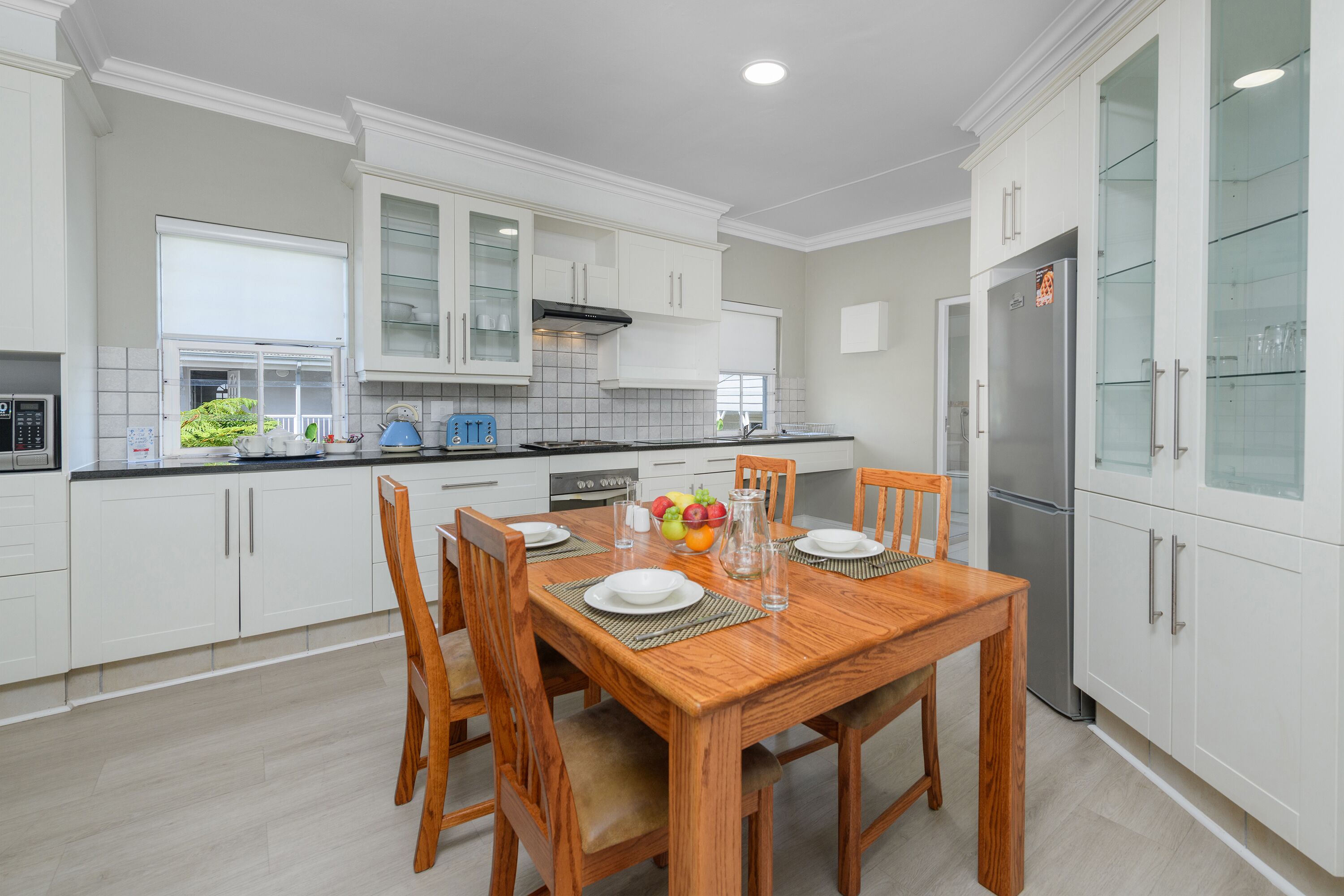 A modern kitchen with white cabinetry, a wooden dining table, and a stainless steel refrigerator.