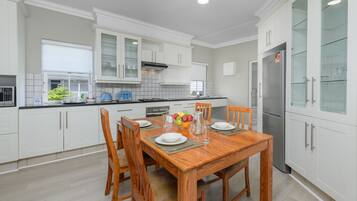 A modern kitchen with white cabinetry, a wooden dining table, and a stainless steel refrigerator.