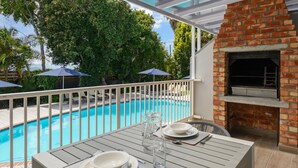 Um alpendre à beira da piscina com uma mesa posta para refeições, uma lareira de tijolos e vista para a piscina.
