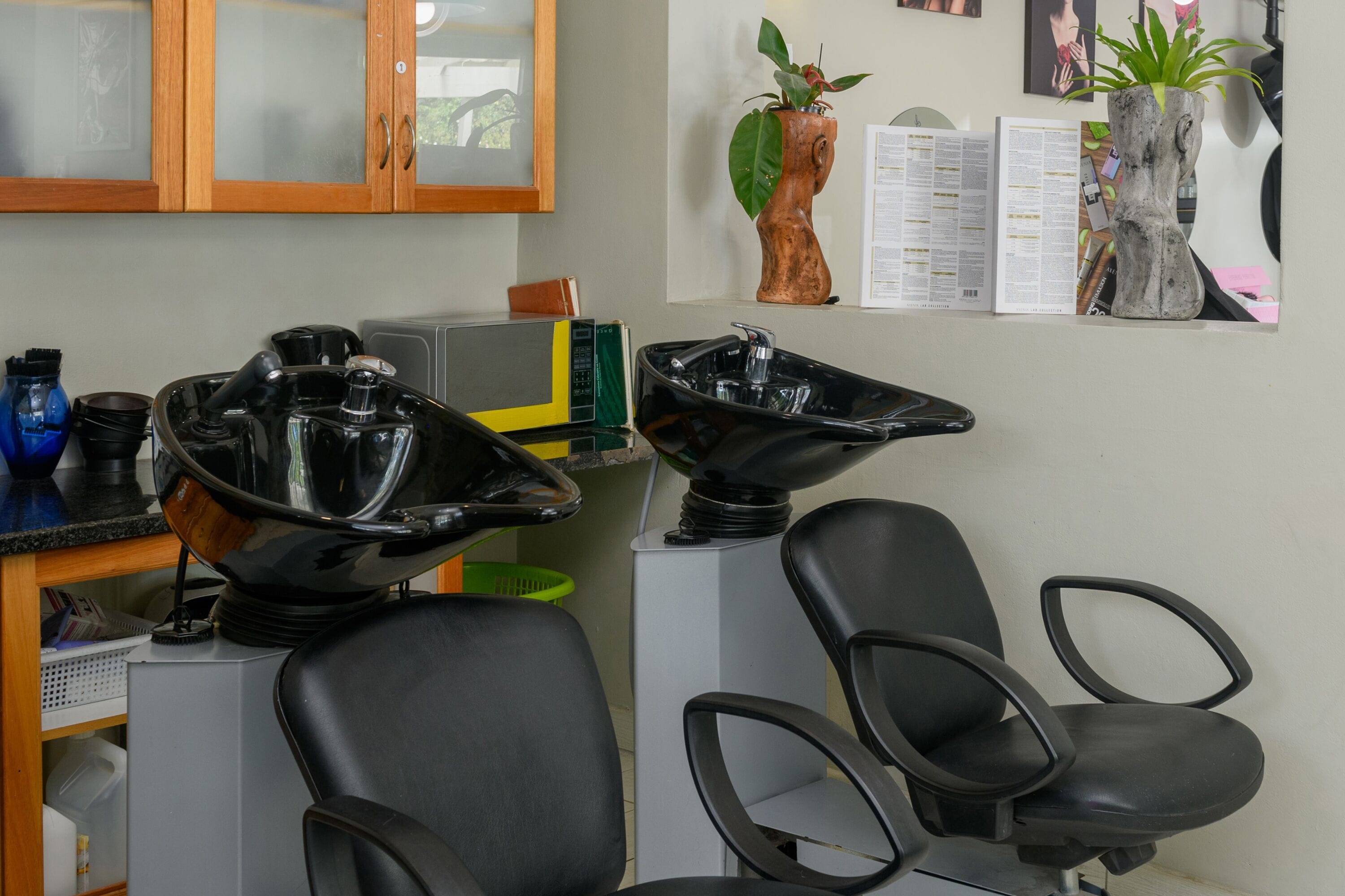 A salon with black salon chairs, a hair washing station, and a wooden cabinet with glass doors.