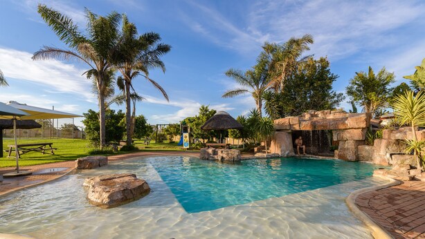 Piscina cristalina com formações rochosas e palmeiras.