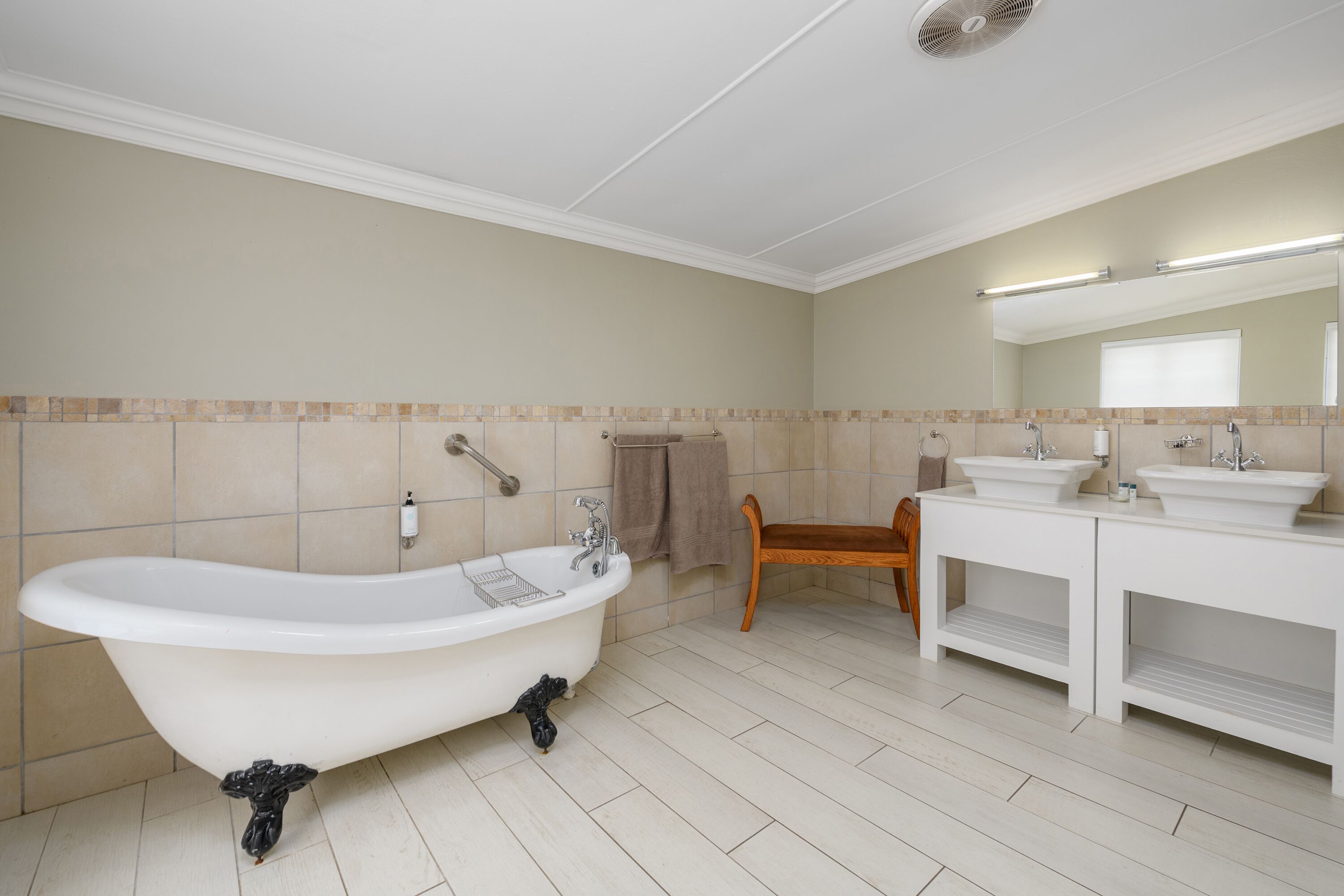 A bathroom with a freestanding bathtub, a wooden bench, and a double sink vanity.