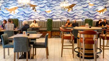 A restaurant with a wave-themed wall, round tables, and various seating options including booths and bar stools.