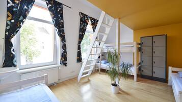 Ein Schlafzimmer mit Etagenbett, Blumentopf, Heizkörper, Kleiderschrank und einem Fenster mit Vorhängen.