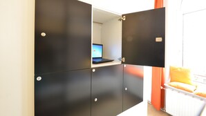 A room with a black wardrobe, a laptop on a shelf, and a window with orange curtains. - Townside Hostel Bremen (Bremen)