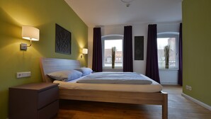 A bedroom with a wooden bed, a nightstand, a wall-mounted lamp, and a window with curtains. - Townside Hostel Bremen (Bremen)