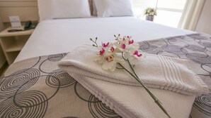 A neatly made bed with white linens, a decorative pillow, and a bouquet of white flowers on the bedspread. - Verona Hplus Long Stay (Lago Norte)