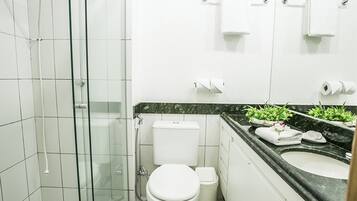 Een moderne badkamer met een glazen douchecabine, toilet, wastafel en een marmeren aanrechtblad.