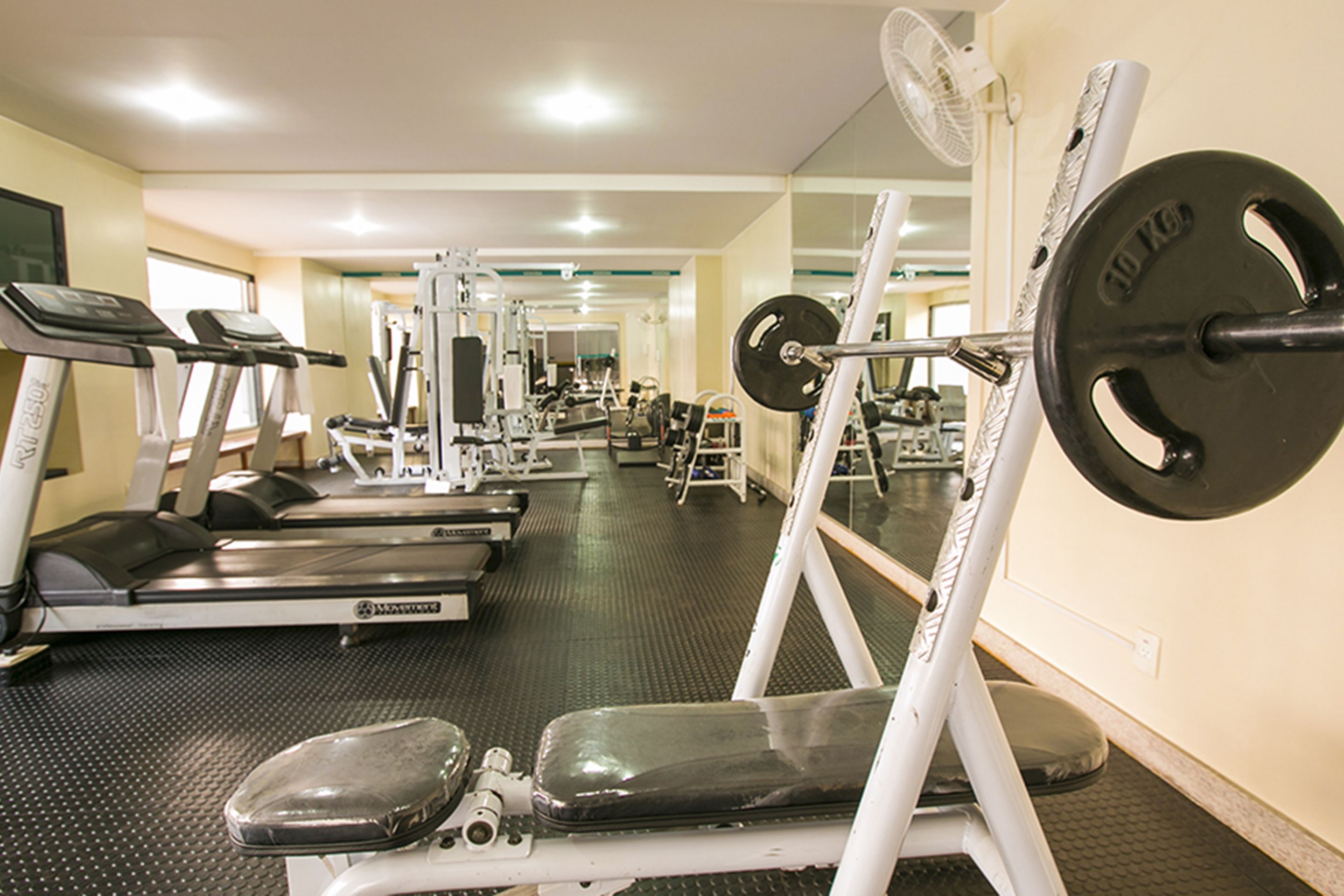 Une salle de sport équipée de tapis de course, d’appareils de musculation et d’un mur recouvert de miroirs.