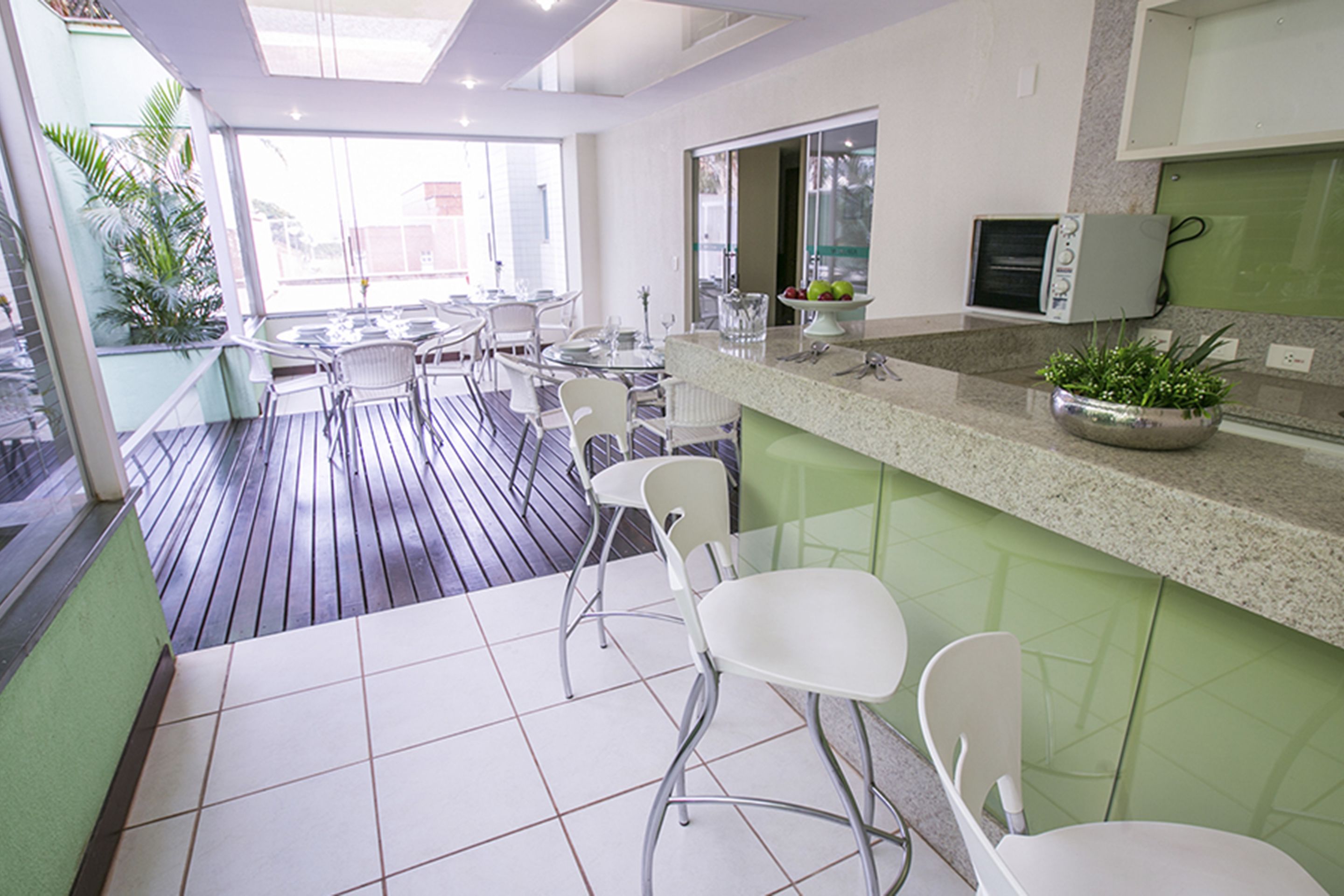 A modern kitchen with a bar area, green cabinets, and a large window.