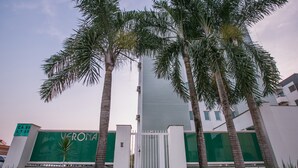 A gated entrance with palm trees, a sign reading "VERONA," and a modern building in the background. - Verona Hplus Long Stay (Lago Norte)