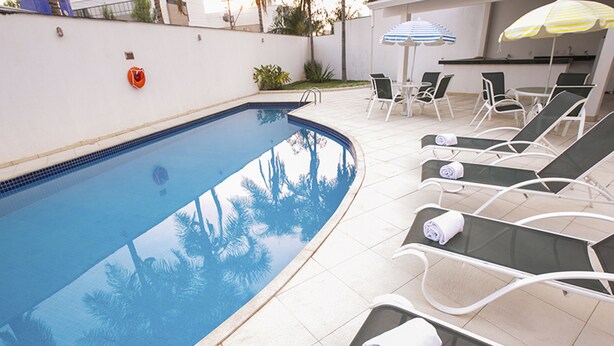 A swimming pool with lounge chairs and umbrellas. - Verona Hplus Long Stay (Lago Norte)