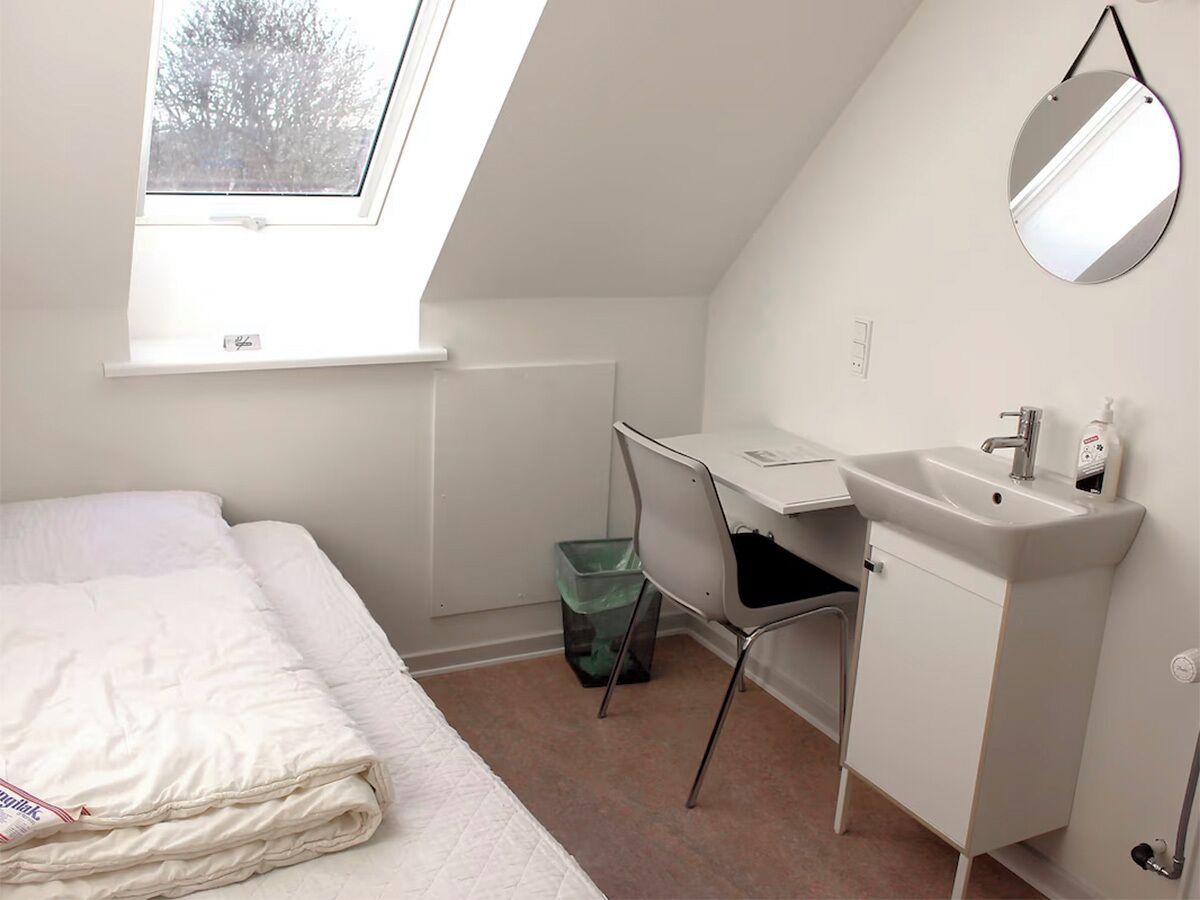 A small, well-lit room with a bed, a desk, and a sink.