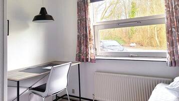 A room with a desk, chair, radiator, and a window with curtains.