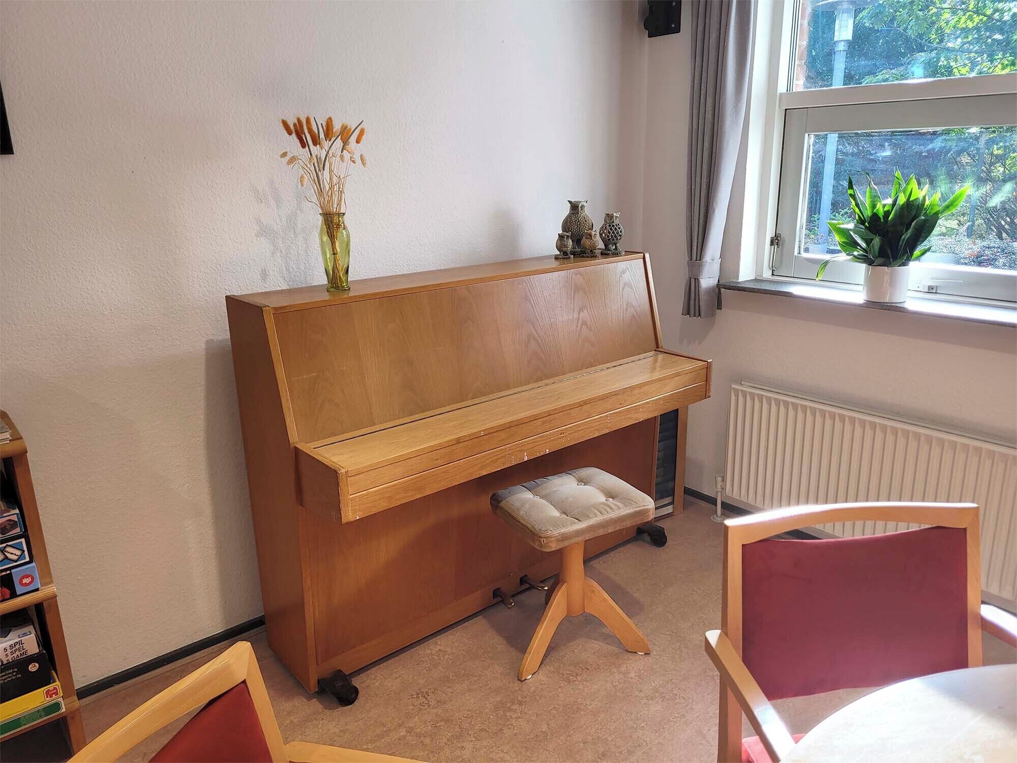 Un piano de madera con un banco, una mesita y un ventanal con vistas al verdor.