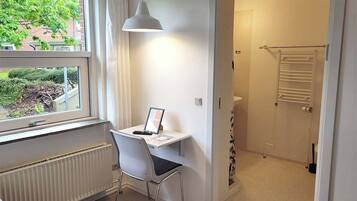 Une chambre d’hôtel équipée d’un bureau, d’une chaise, d’un radiateur, d’une fenêtre et offrant une vue sur la verdure environnante.