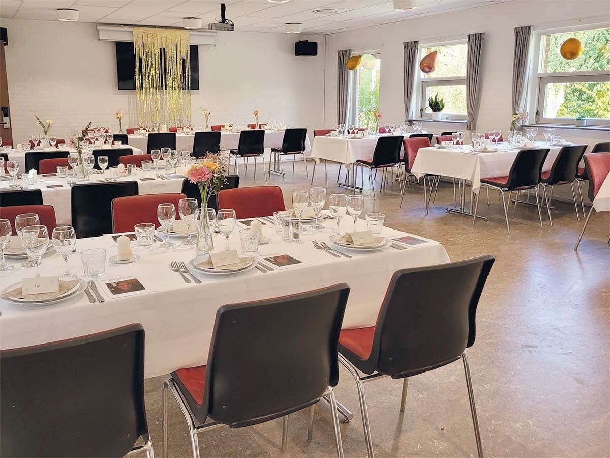 Een balzaal met ronde tafels gedekt voor het diner, stoelen en een podium met een scherm.