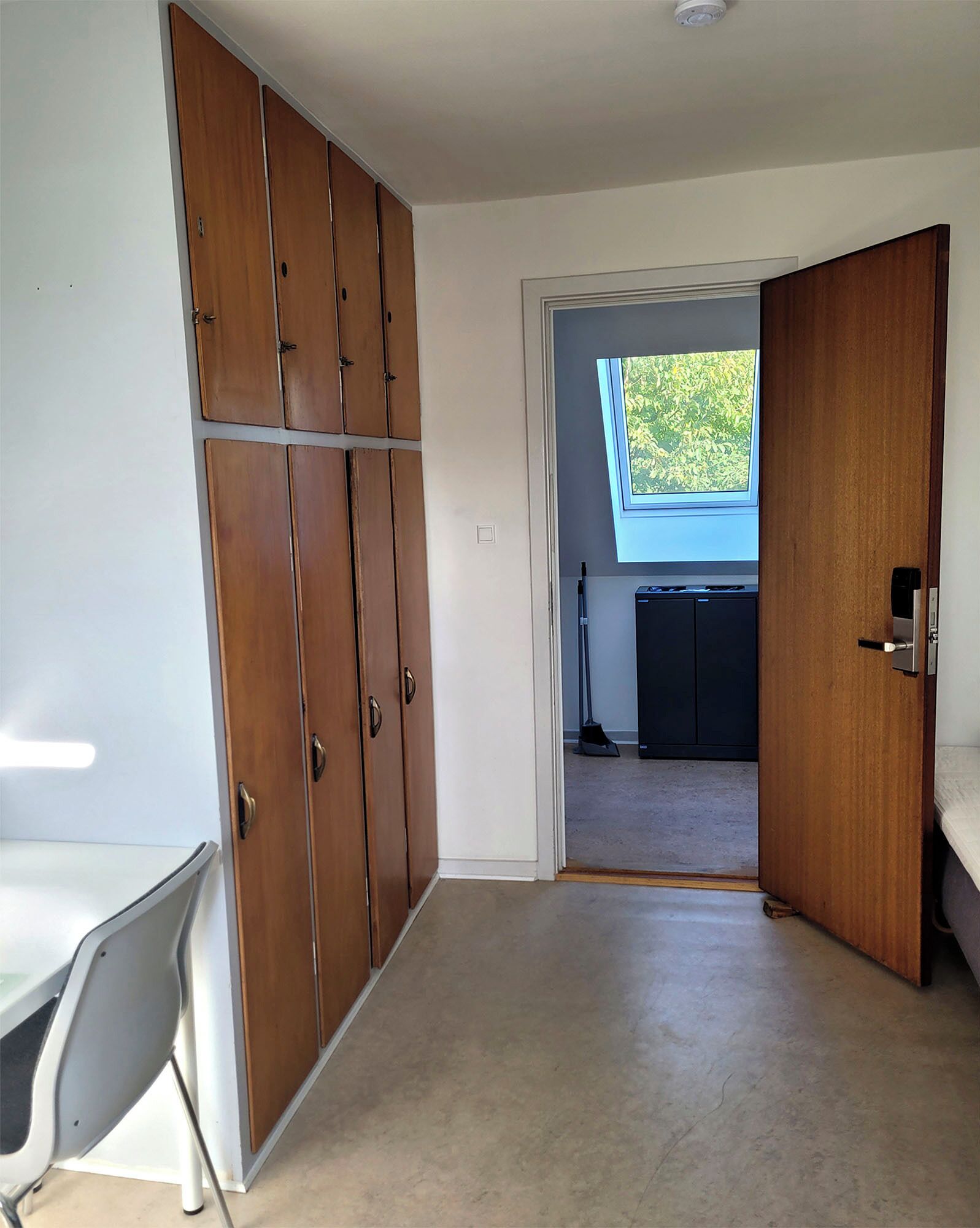 Una stanza con un armadio in legno, una scrivania e vista su un angolo cucina attraverso una porta aperta.