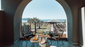 A balcony with wicker chairs and a table, overlooking a beach and resort area. - Eliros Mare Beachfront Poem Hotel (Apokoronas)