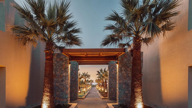 A pathway flanked by palm trees and stone pillars leading to a covered area. - Eliros Mare Beachfront Poem Hotel (Apokoronas)