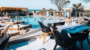 A poolside area with lounge chairs, umbrellas, and a table with chairs. - Eliros Mare Beachfront Poem Hotel (Apokoronas)