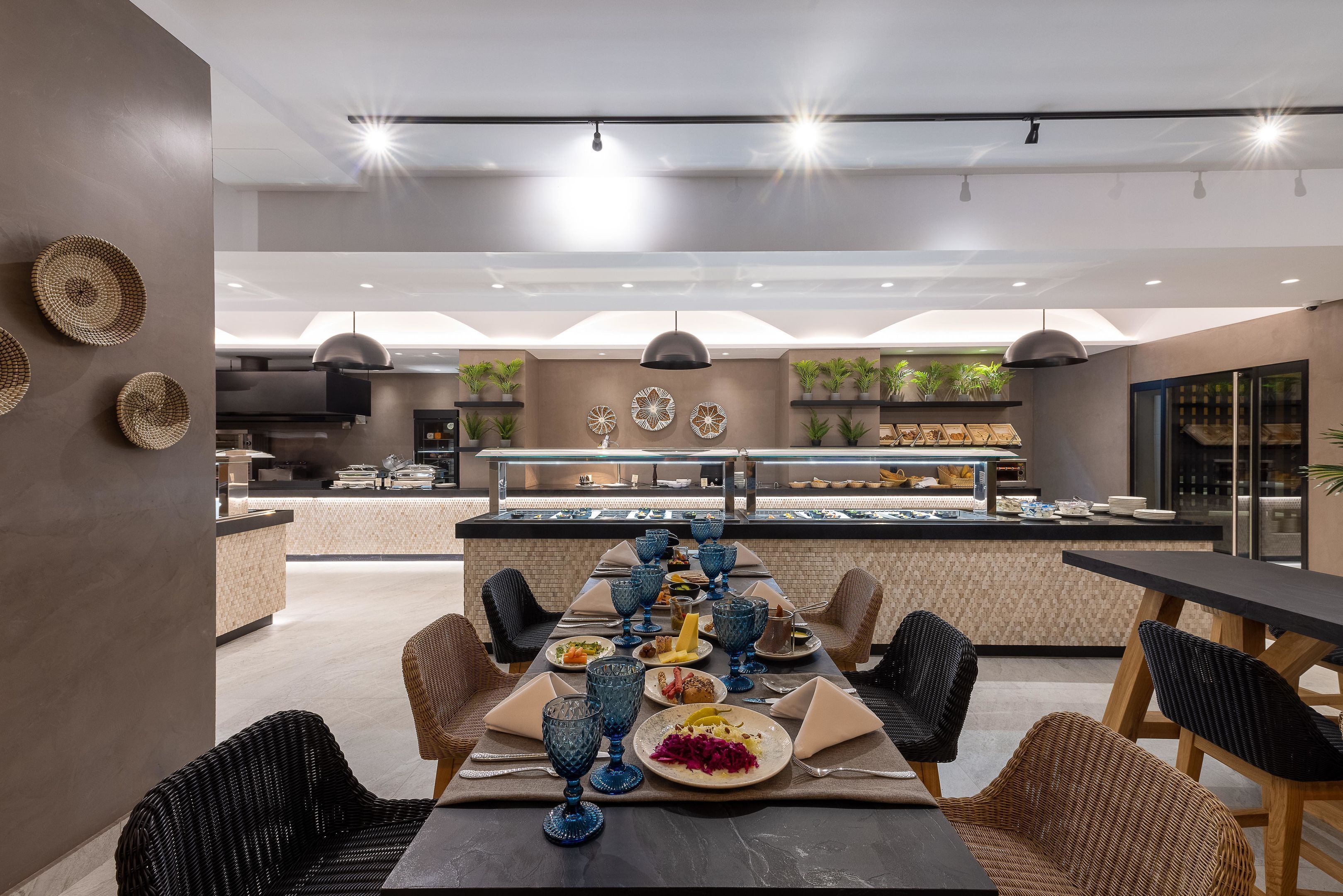 A modern dining area with a long table, wicker chairs, and blue glassware.