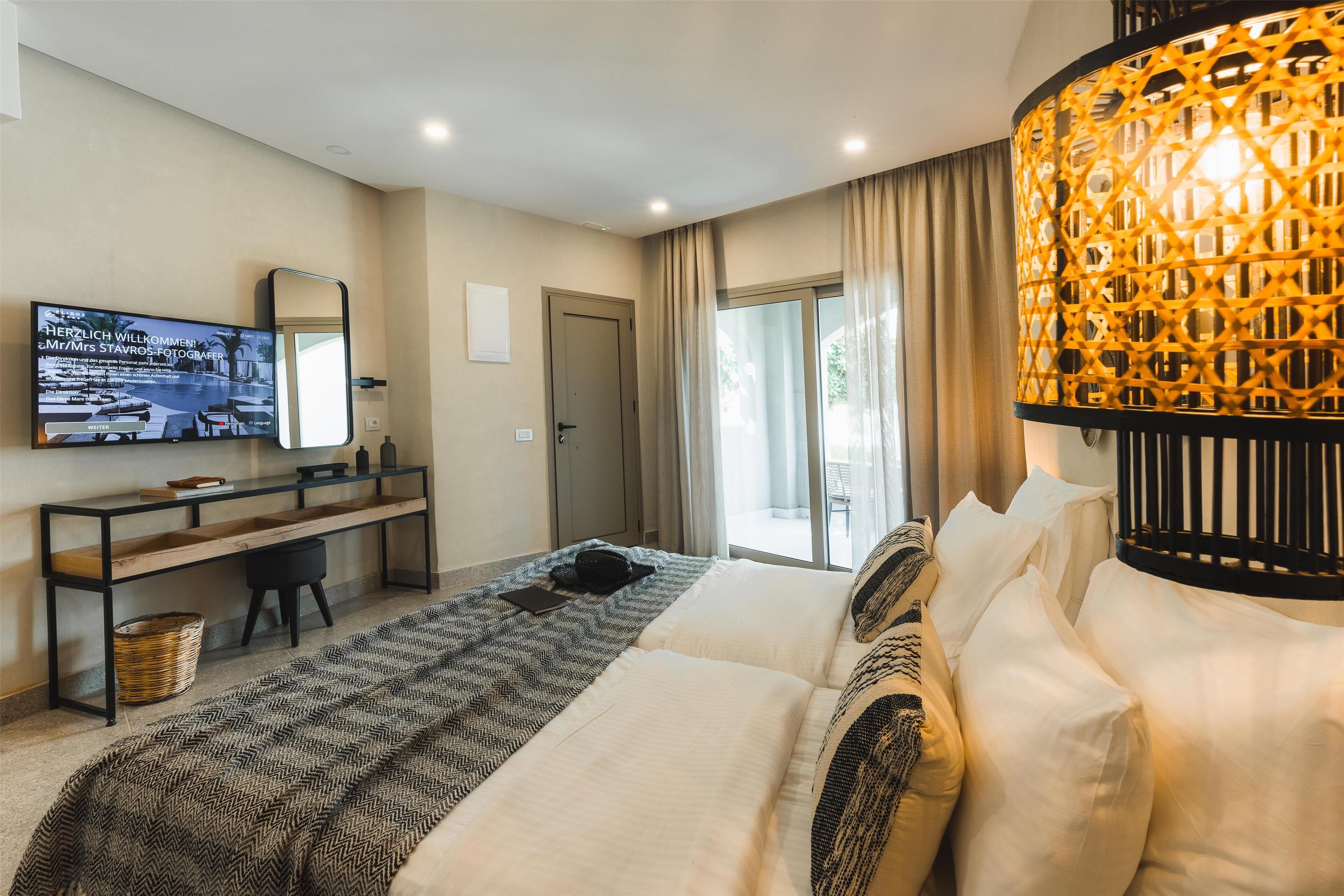 Ein modernes Hotelzimmer mit einem großen Bett, einem Schreibtisch mit Fernseher, einem großen Fenster und einer dekorativen Lampe.
