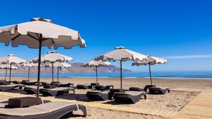 A beach with lounge chairs and umbrellas, a wooden boardwalk, and a clear blue sky. - Eliros Mare Beachfront Poem Hotel (Apokoronas)