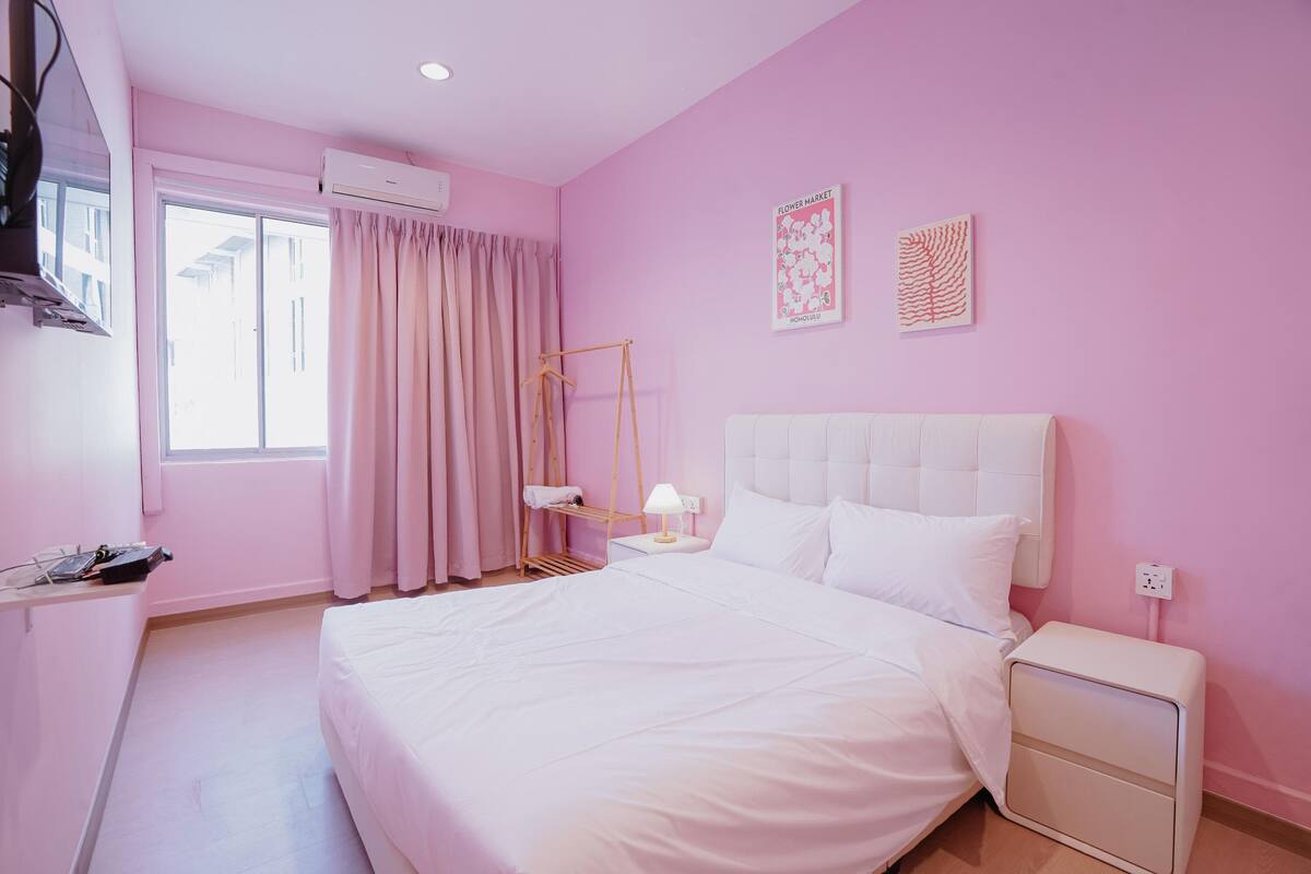 A pink-themed hotel room with a bed, bedside table, and a window with curtains.
