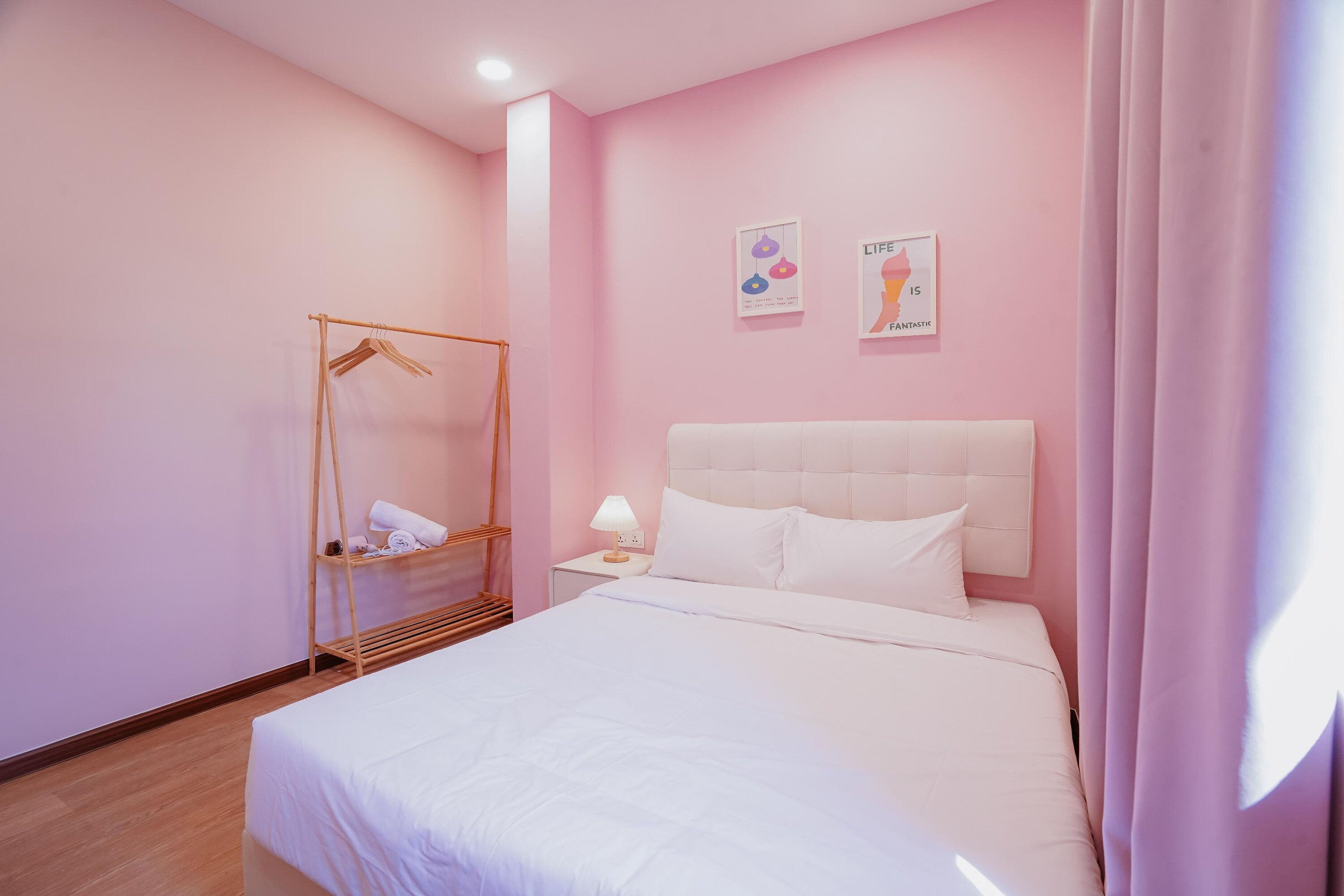 A bedroom with a bed, a bedside table with a lamp, a wooden hanger rack, and two wall art pieces.
