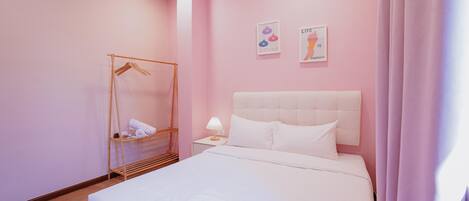 A bedroom with a bed, a bedside table with a lamp, a wooden hanger rack, and two wall art pieces.