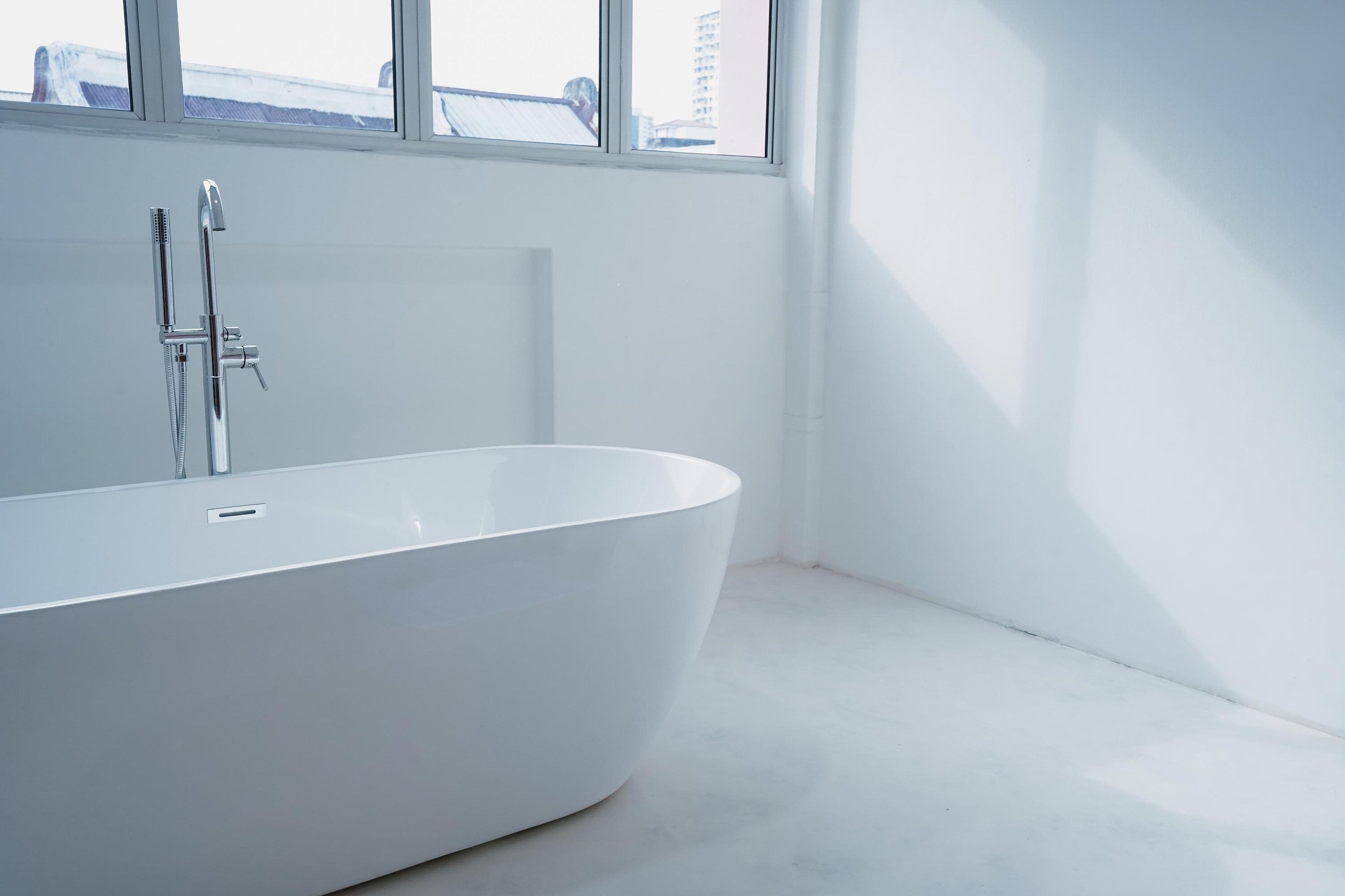 Un baño moderno con una bañera independiente, un cabezal de ducha y una ventana que ofrece vistas de edificios.