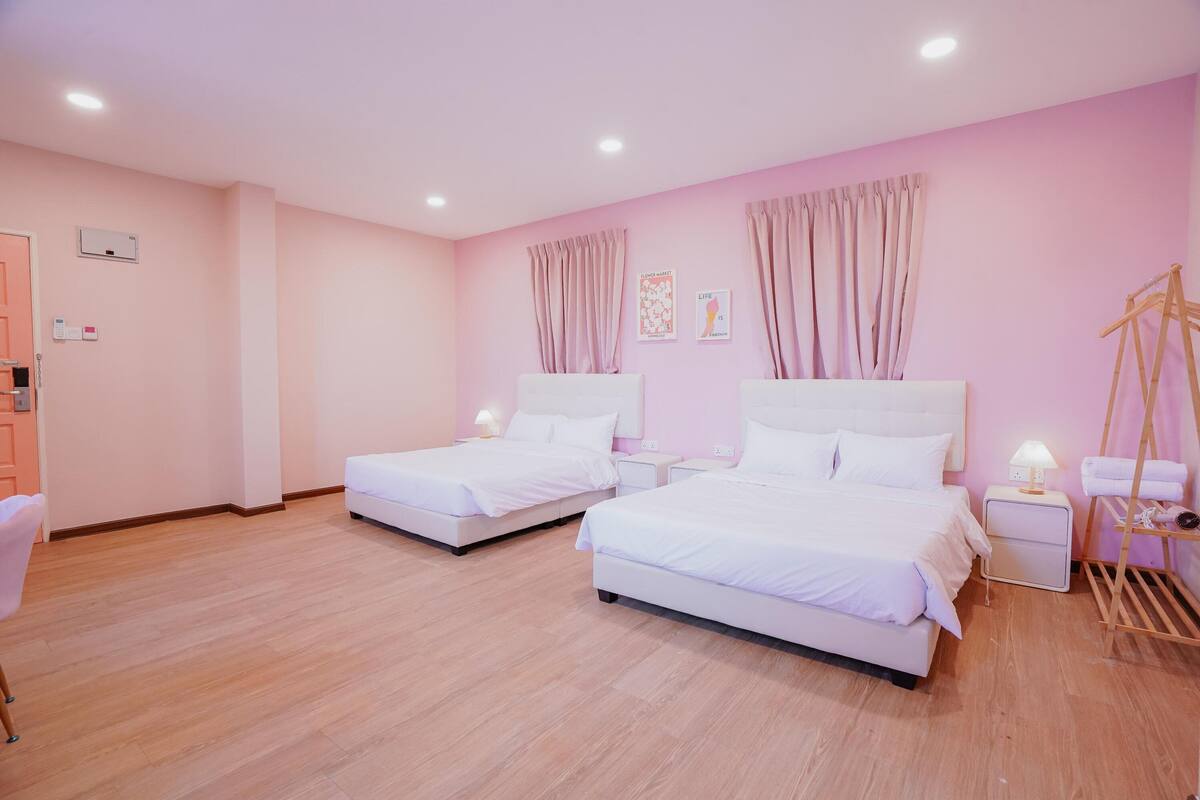 A hotel room with two beds, wooden flooring, a wardrobe, and a bedside table with a lamp.