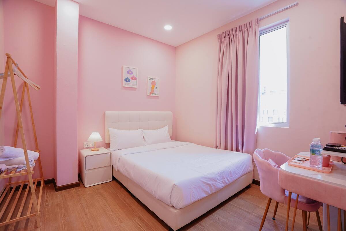 A pink-themed bedroom with a bed, bedside table, lamp, and a chair.