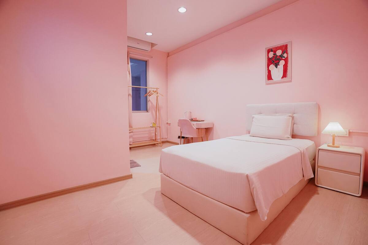A pink-themed bedroom with a bed, bedside tables, a desk, and a chair.