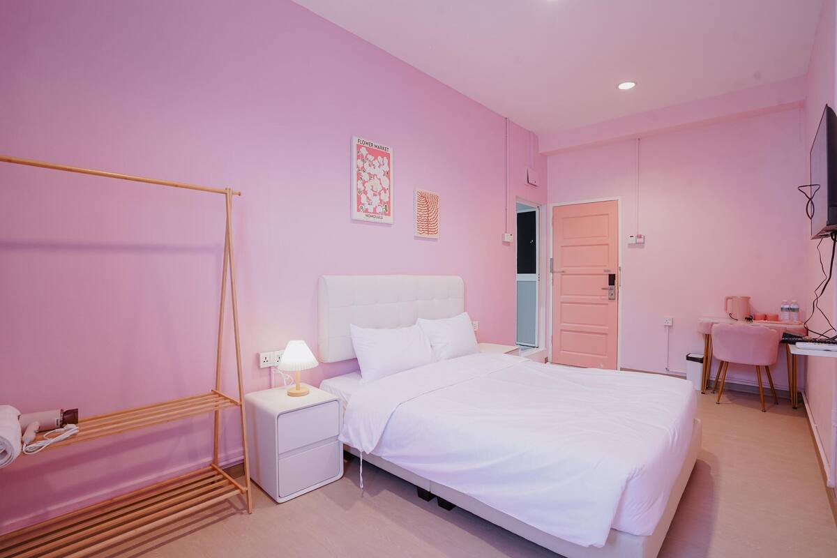 A pink-themed bedroom with a bed, bedside table, lamp, and a wooden rack.