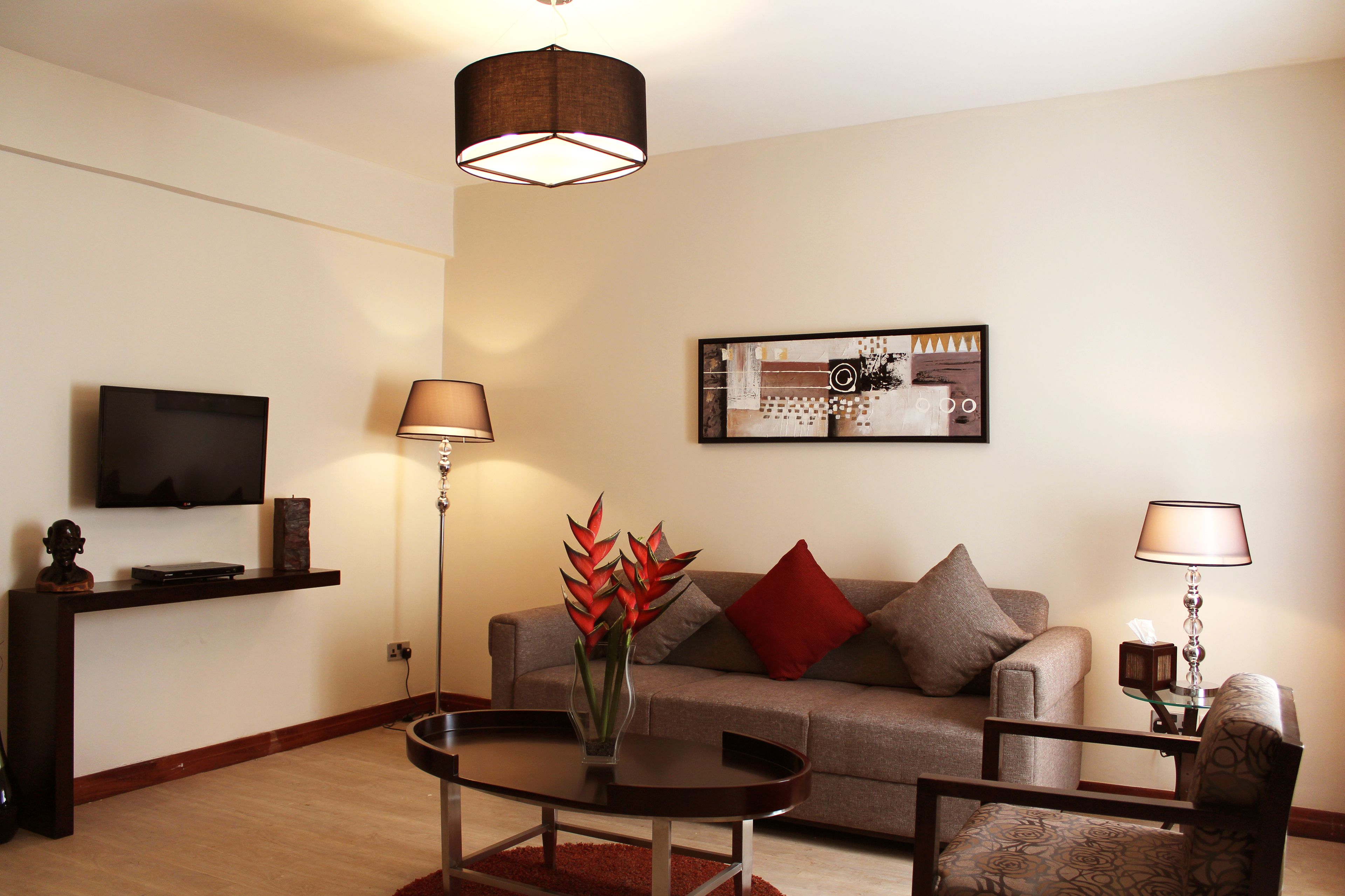 A modern living room with a flat-screen TV, a coffee table, a sofa with red cushions, and a floor lamp.