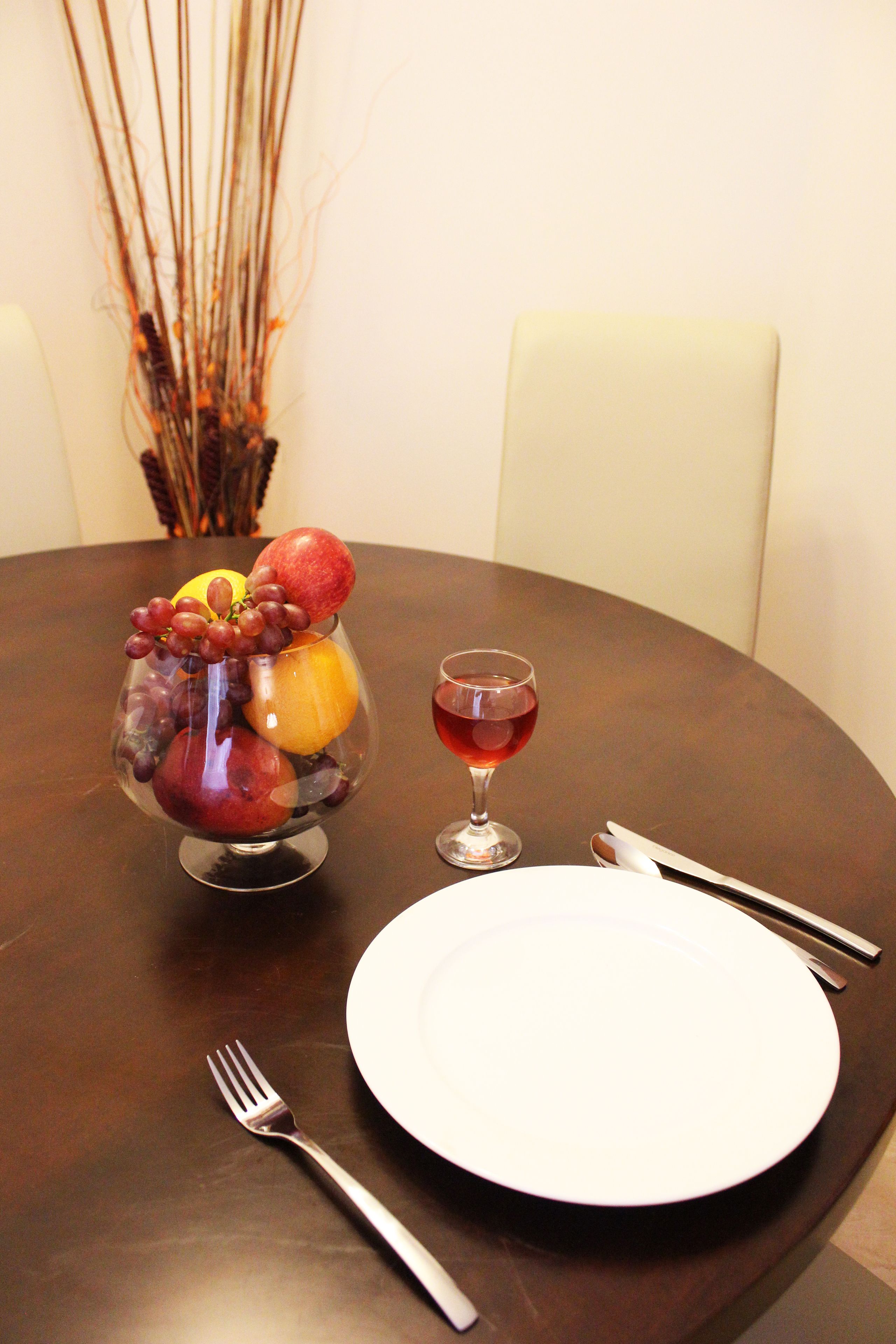 A dining table with a fruit bowl, a wine glass, and cutlery.