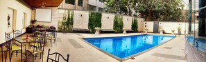 A swimming pool with a tiled deck, surrounded by a patio area with outdoor seating.