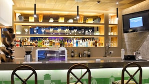 A bar area with wooden ceiling, shelves with bottles, a TV screen, and two bar stools.