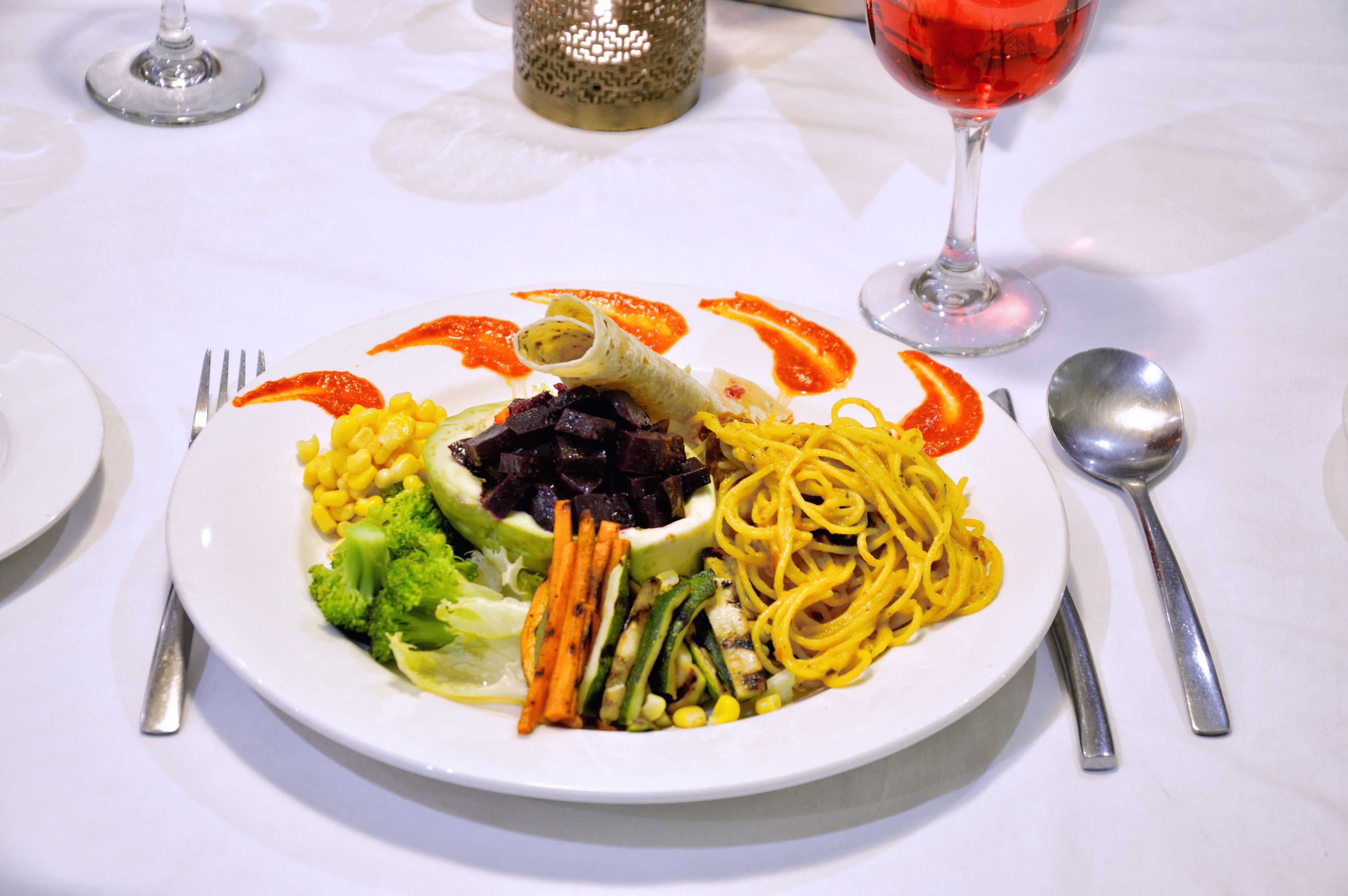 A plate of food with vegetables and noodles, accompanied by a glass of red wine and a candle on a table.